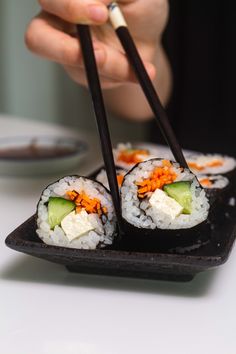 a person holding chopsticks over some sushi