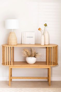 a wooden table with two vases and a book on it next to a lamp