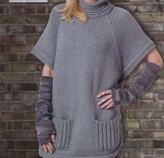 a woman standing in front of a brick wall wearing a gray sweater and matching gloves