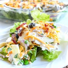 a white plate topped with salad covered in cheese and dressing next to a casserole dish