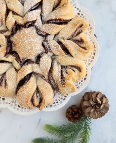 a white plate topped with pastries covered in powdered sugar next to pine cones