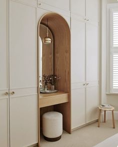 a room with white cupboards and an arched mirror on the wall next to a stool