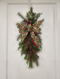 a green and red bow hanging on a door with pine cones, berries and evergreen leaves