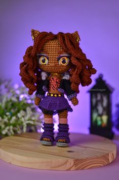 a crocheted doll is standing on a wooden board