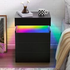 a black night stand with two drawers and a rainbow light on the bottom shelf next to it