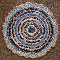 a crocheted rug is laying on the floor with blue and pink yarns