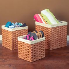 two baskets with shoes in them sitting on a wooden floor next to a brown wall