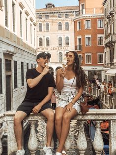 two people sitting on a ledge eating ice cream and talking to each other in the city