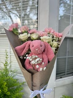 a pink teddy bear sitting inside of a bouquet of white and pink flowers in front of a house