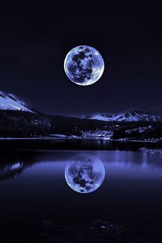 a full moon is seen over a mountain lake at night with mountains in the background