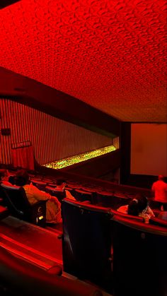 an auditorium with red lighting and people sitting in the seats