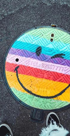 a manhole cover with a smiley face painted on it's side and feet standing next to it