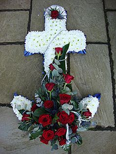 a cross with red roses and white daisies on the ground in front of it