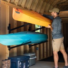 a man standing next to a yellow and blue kayak in a room with wooden walls