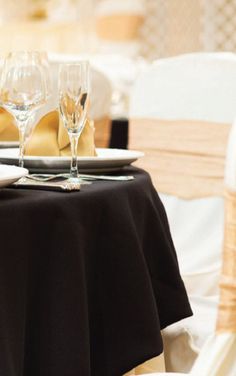 the table is set with white and black linens, gold place settings and wine glasses