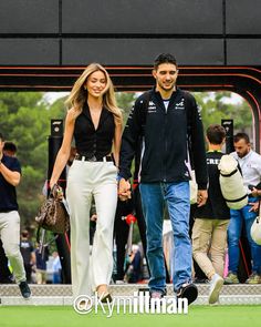 a man and woman holding hands while walking on the grass in front of a crowd