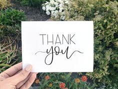 someone holding up a card with the words thank you on it in front of some flowers