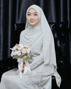 a woman in a white hijab holding a bouquet of flowers on a black chair