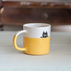 a yellow and white coffee cup with a black cat on it's side sitting on a table