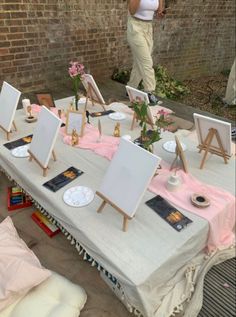 a table with several easels and paintings on it, in front of a brick wall