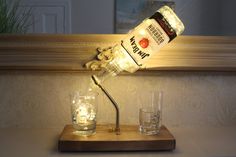 a lighted bottle lamp sitting on top of a wooden table next to two shot glasses