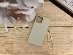 a white phone case sitting on top of a wooden table next to a flower and beaded necklace