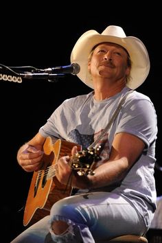 a man with a cowboy hat is playing an acoustic guitar