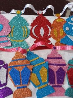 some paper cutouts are hanging from a string on a piece of white fabric with pink and blue glitters