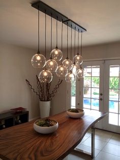 a wooden table topped with bowls filled with plants and lights hanging from it's ceiling