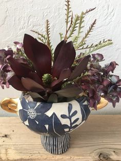 a blue and white vase filled with purple flowers on top of a wooden table next to a wall