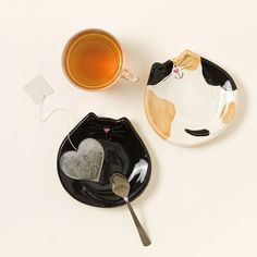 two black and white plates with cats on them next to a cup of tea or coffee