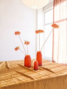 three vases with flowers in them sitting on a table next to a curtained window