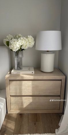 a vase with white flowers sitting on top of a wooden dresser next to a lamp