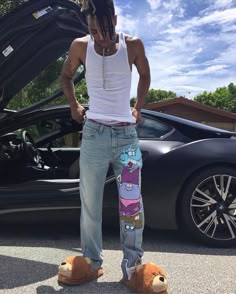 a man with dreadlocks standing in front of a sports car and teddy bear slippers