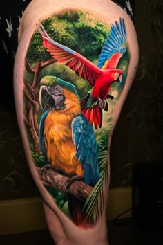 colorful parrots on the back of a woman's thigh with trees and leaves