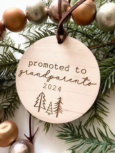 a wooden ornament hanging from a christmas tree with ornaments around it and the words, promote to grandparents