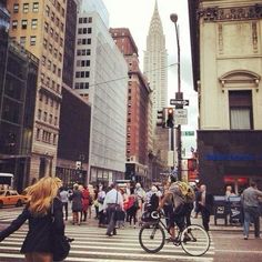 many people are crossing the street in front of tall buildings on a busy city street