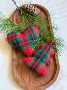 two red and green plaid heart ornaments on a wooden platter with pine cones, needles and evergreen branches