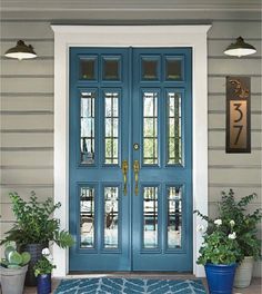 a blue front door with two potted plants on the side and an entrance mat