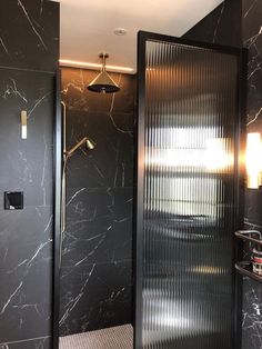 a bathroom with black marble walls and flooring, shower head light on the wall