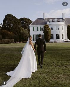 a bride and groom walking in front of a large white house