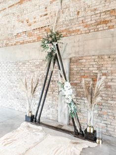 an arrangement of flowers and greenery is placed on the floor in front of a brick wall