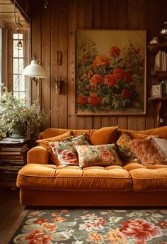 an orange couch in front of a painting on the wall with flowers and plants around it