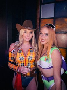 two women dressed in costumes posing for the camera with one holding a drink and another wearing a cowboy hat