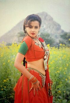 a woman in an orange and green sari posing for the camera with her hands on her hips