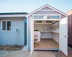 a storage shed with the door open and shelves in it's center, next to two other buildings