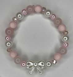 a bracelet with pink and white beads and a silver bow charm on it's side