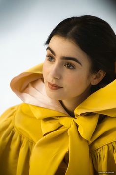 a woman wearing a yellow dress with a large bow around her neck and black hair