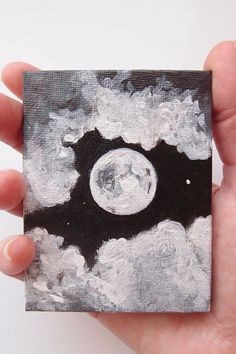 a hand holding up a small square piece of art with the moon in the sky