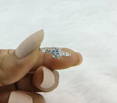 a woman's hand holding a ring with a diamond in it on top of her finger